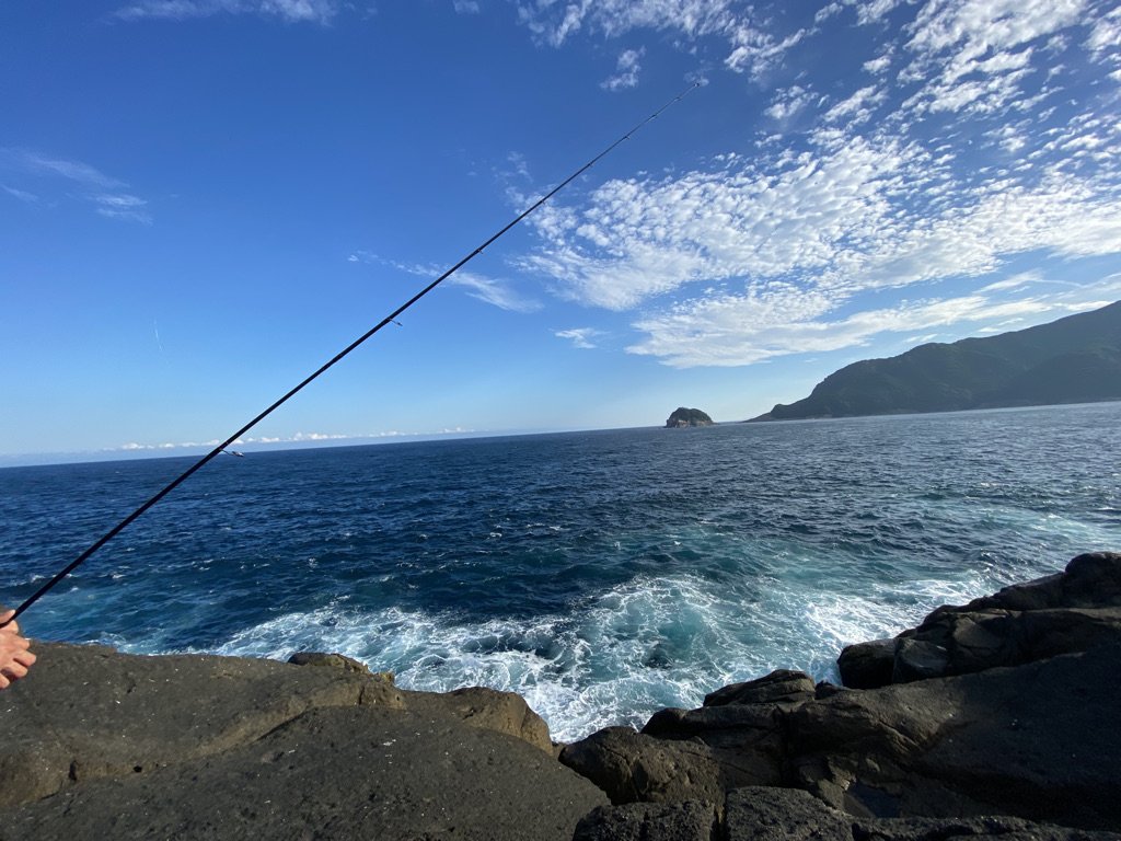 岩場の足元から少し荒れた海で釣りをしている様子