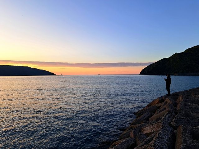 夕暮れの海で釣りをする人のシルエット